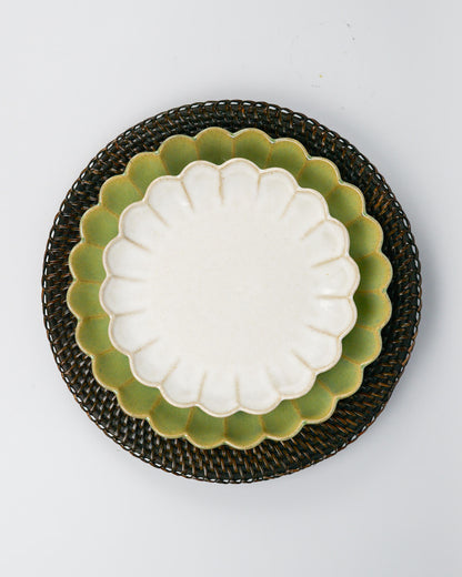 White scalloped dessert plate with green scalloped dinner plate underneath on a rattan placemat against a white background