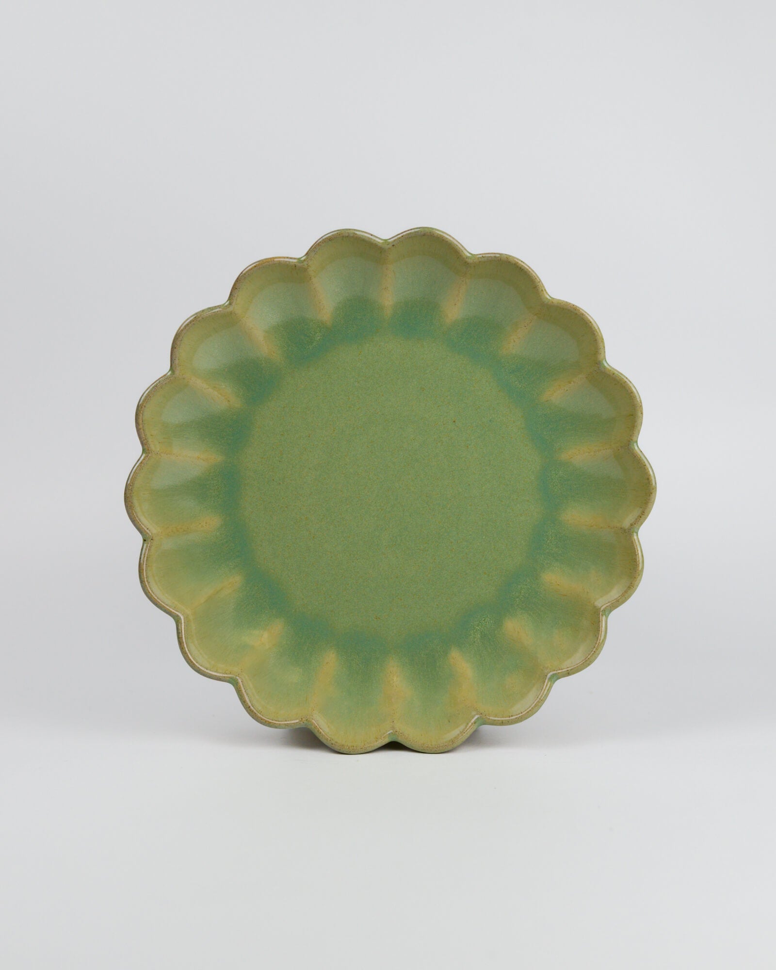 Green ceramic dessert plate with scalloped edge on a white background