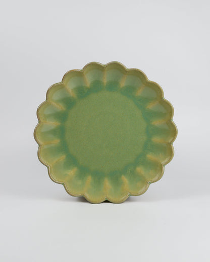 Green ceramic dessert plate with scalloped edge on a white background