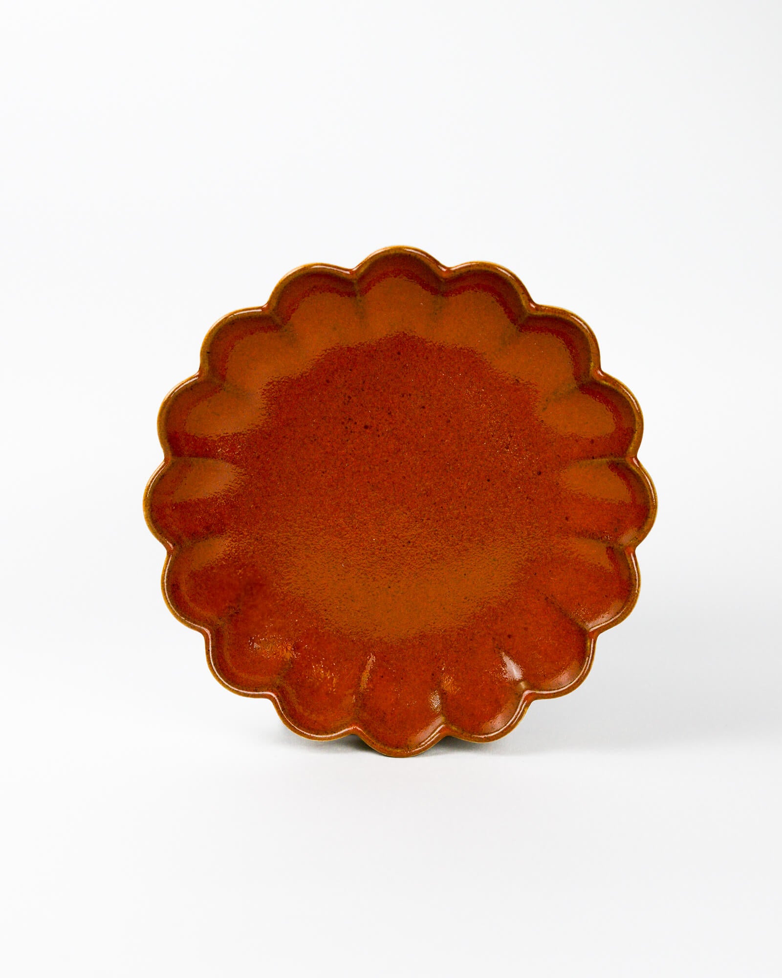 Brown ceramic plate with scalloped edge on a white background