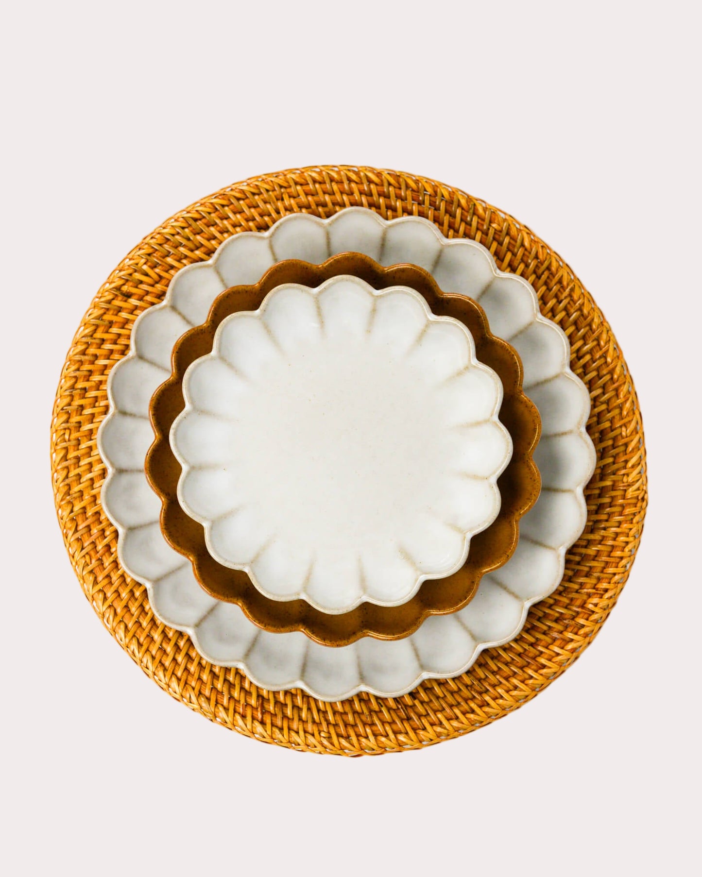 Set of three scalloped edged stoneware plates with scalloped edges on a woven rattan charger plate