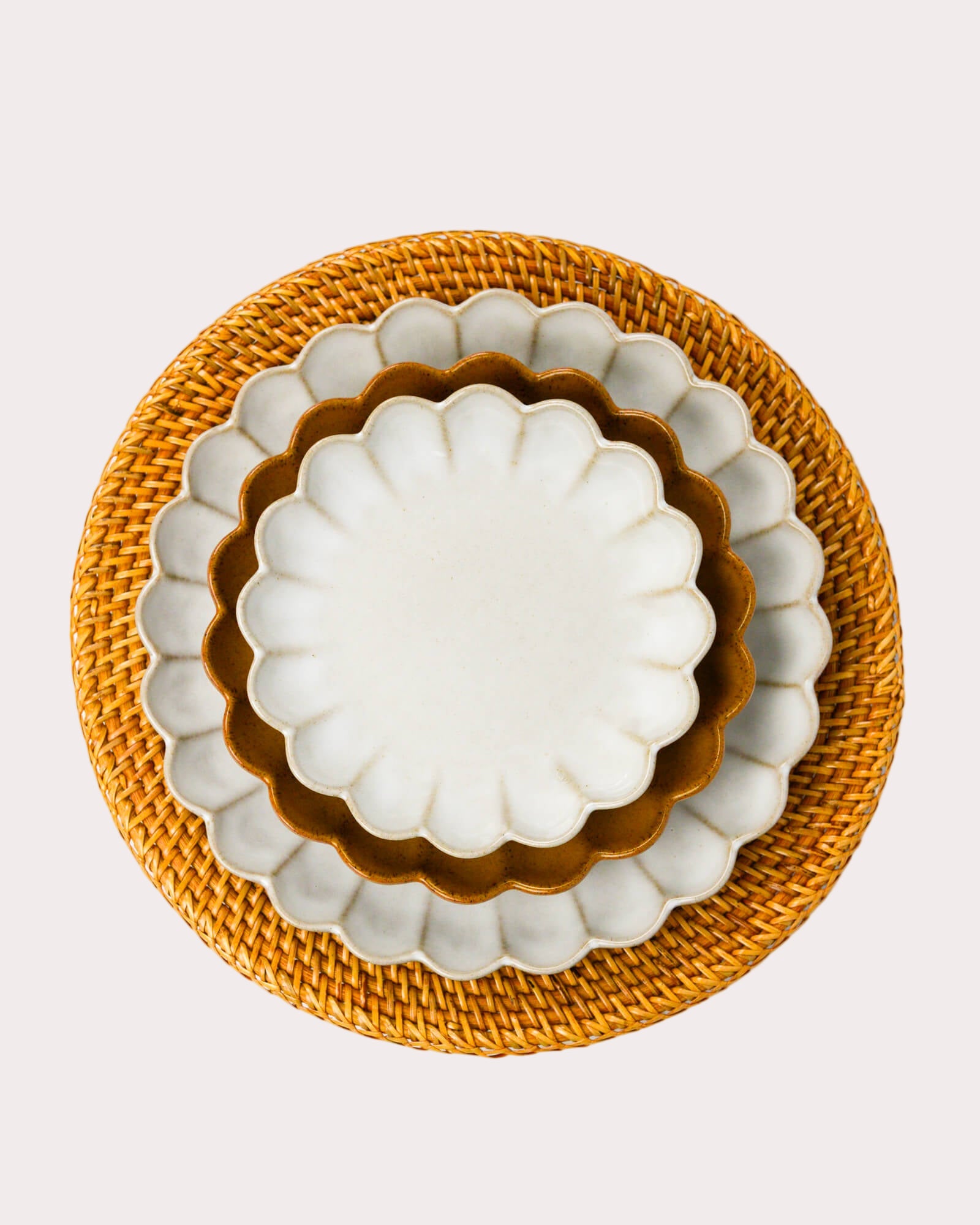 Set of three scalloped edged stoneware plates with scalloped edges on a woven rattan charger plate