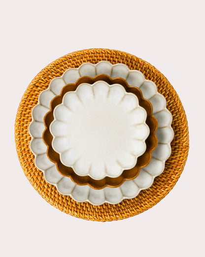 Set of three scalloped edged stoneware plates with scalloped edges on a woven rattan charger plate