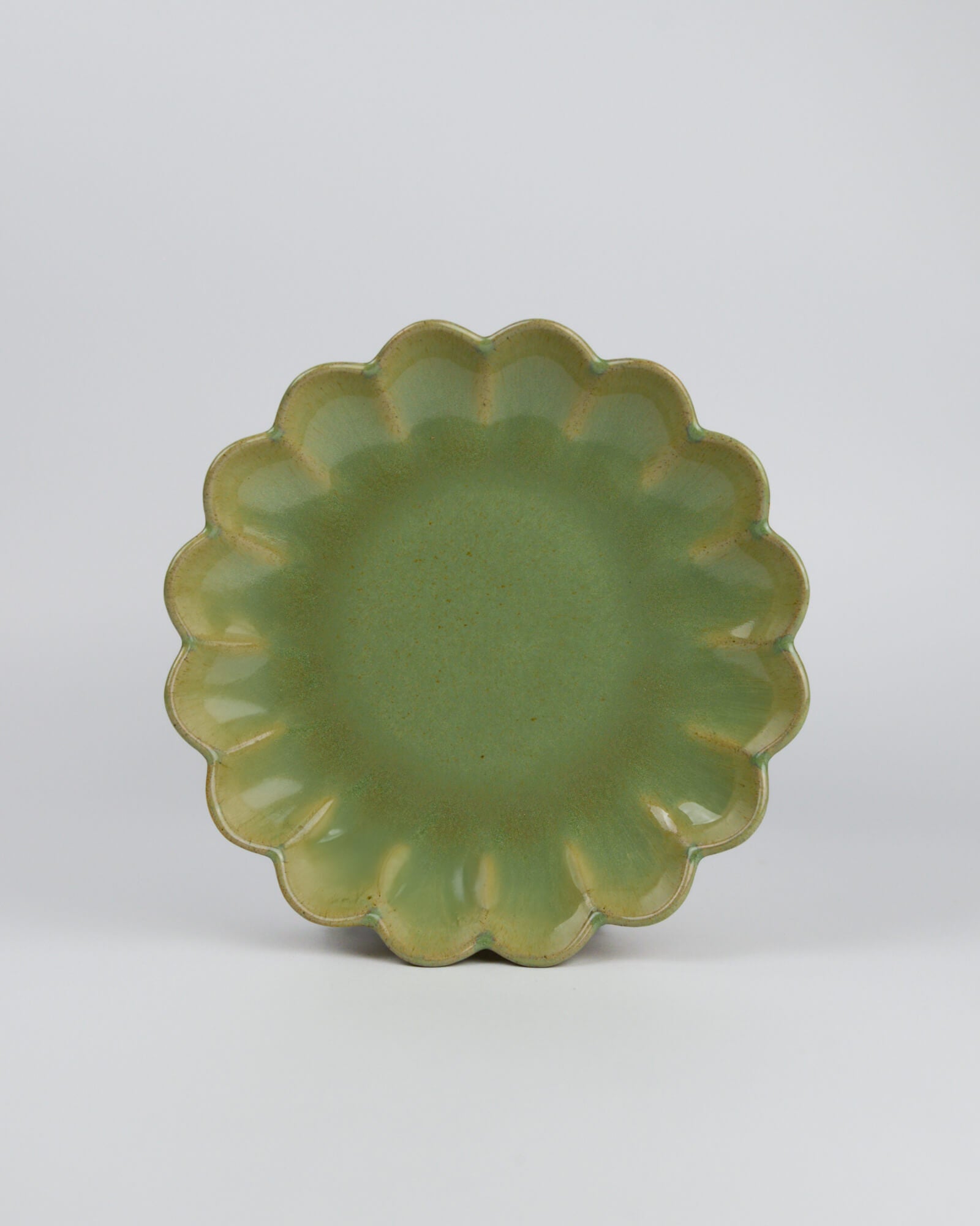 Green ceramic appetiser plate with scalloped edge on a white background