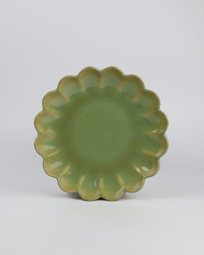 Green ceramic appetiser plate with scalloped edge on a white background
