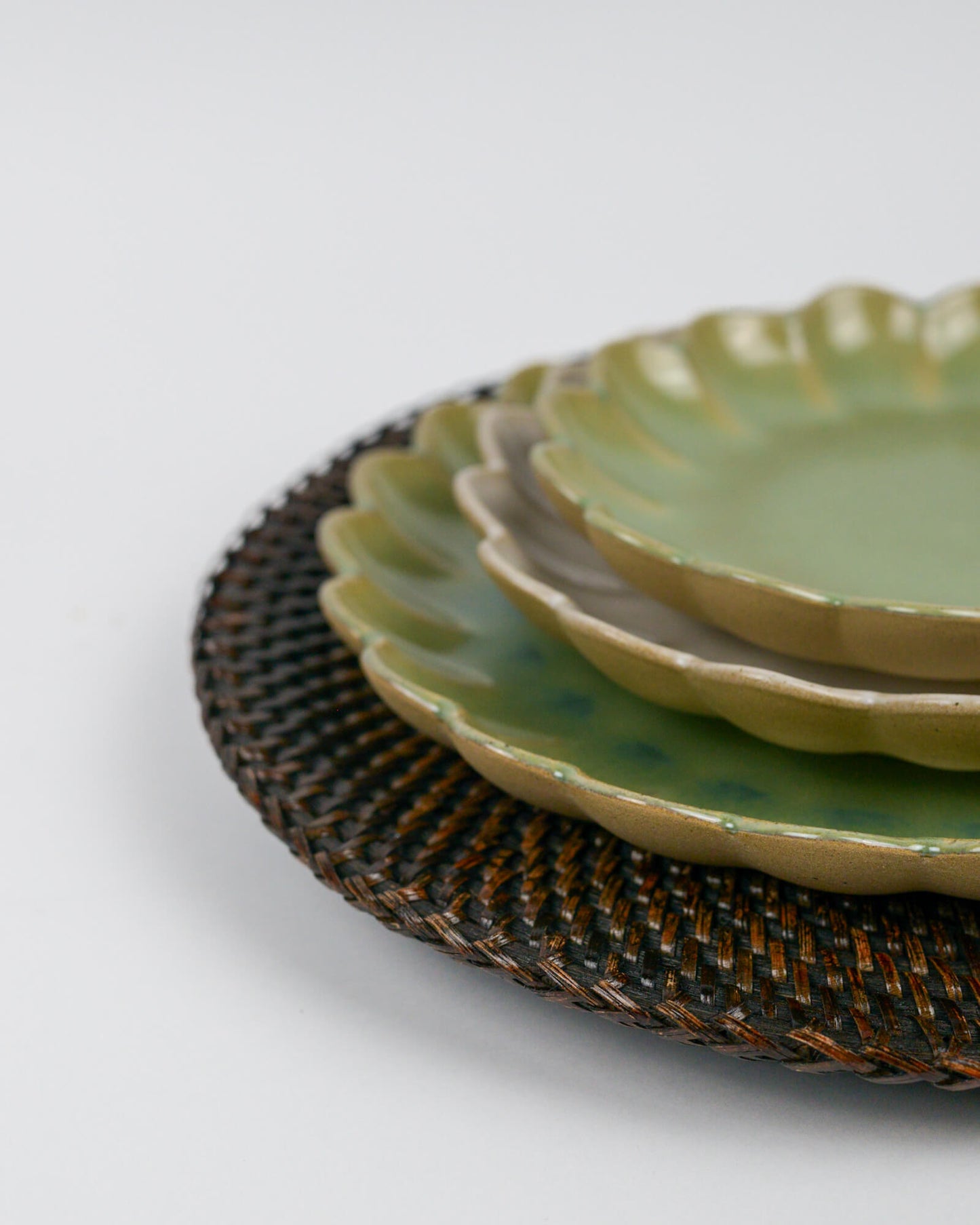 Stack of green ceramic plates on a rattan charger plate with a white background