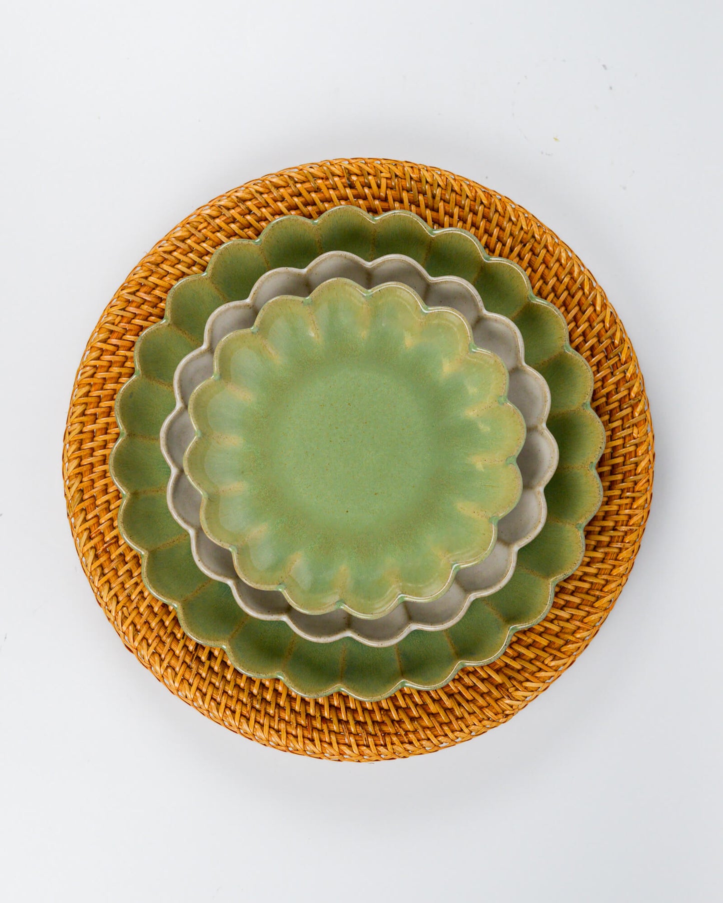 Set of green ceramic plates with scalloped edges on a rattan charger plate against a white background 