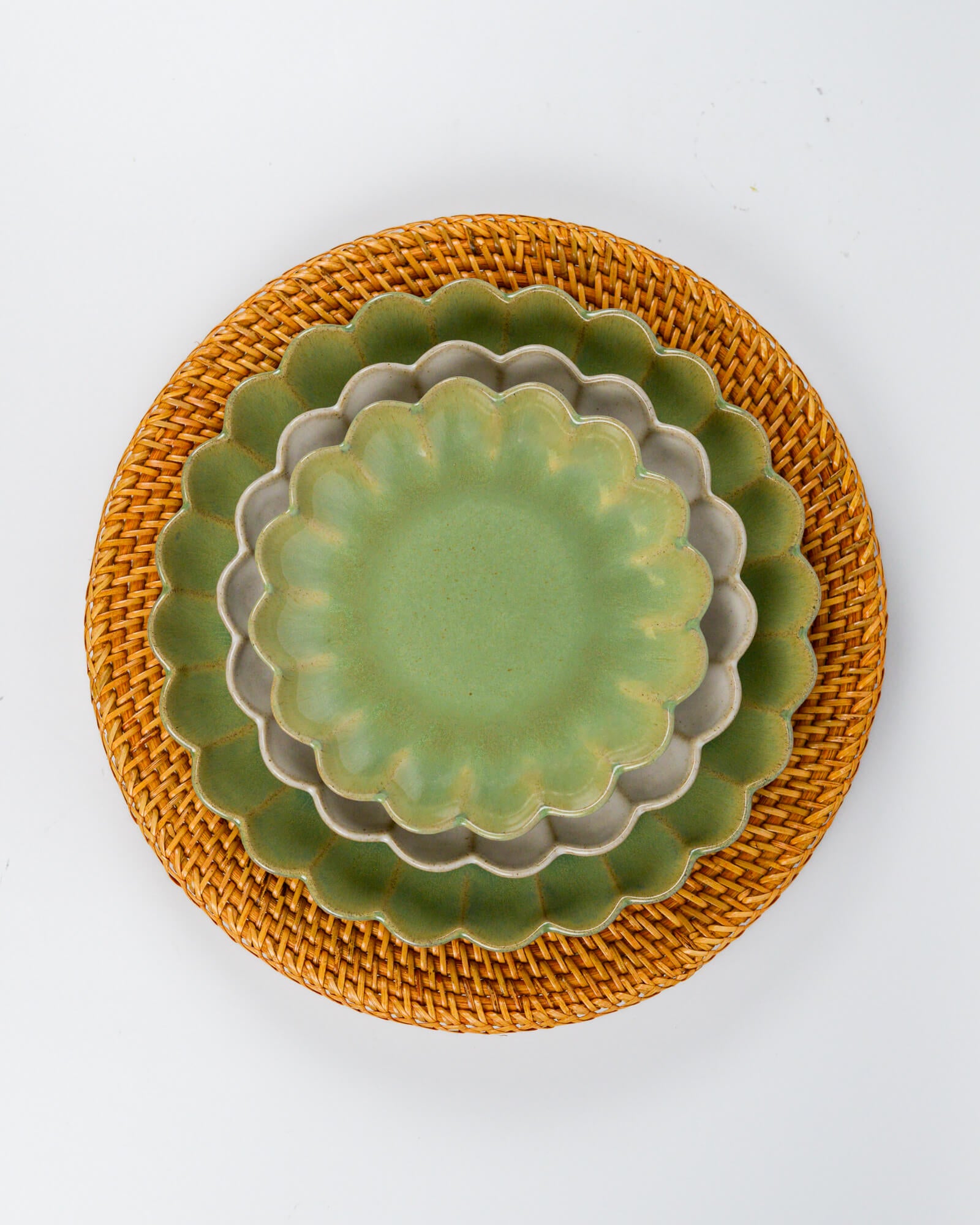 Set of green ceramic plates with scalloped edges on a rattan charger plate against a white background 