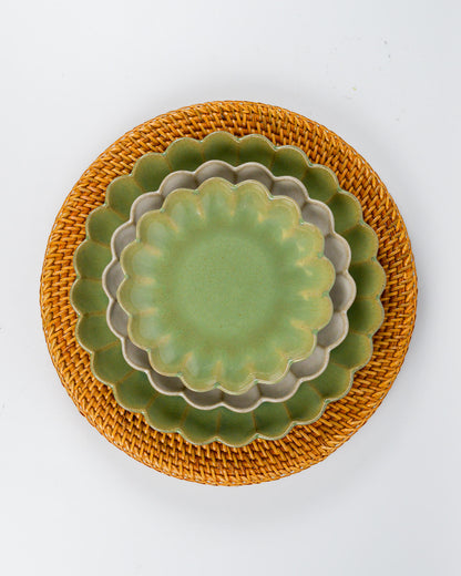 Set of green ceramic plates with scalloped edges on a rattan charger plate against a white background 