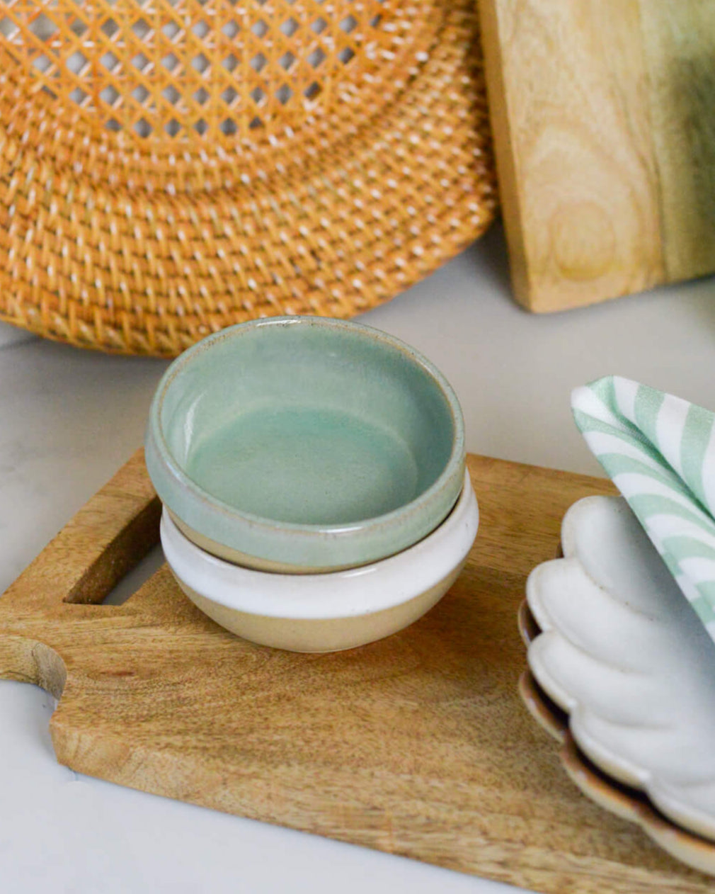 Stack of ceramic stoneware dipping bowls on a wooden cutting board with a woven mat and striped napkin in the background.