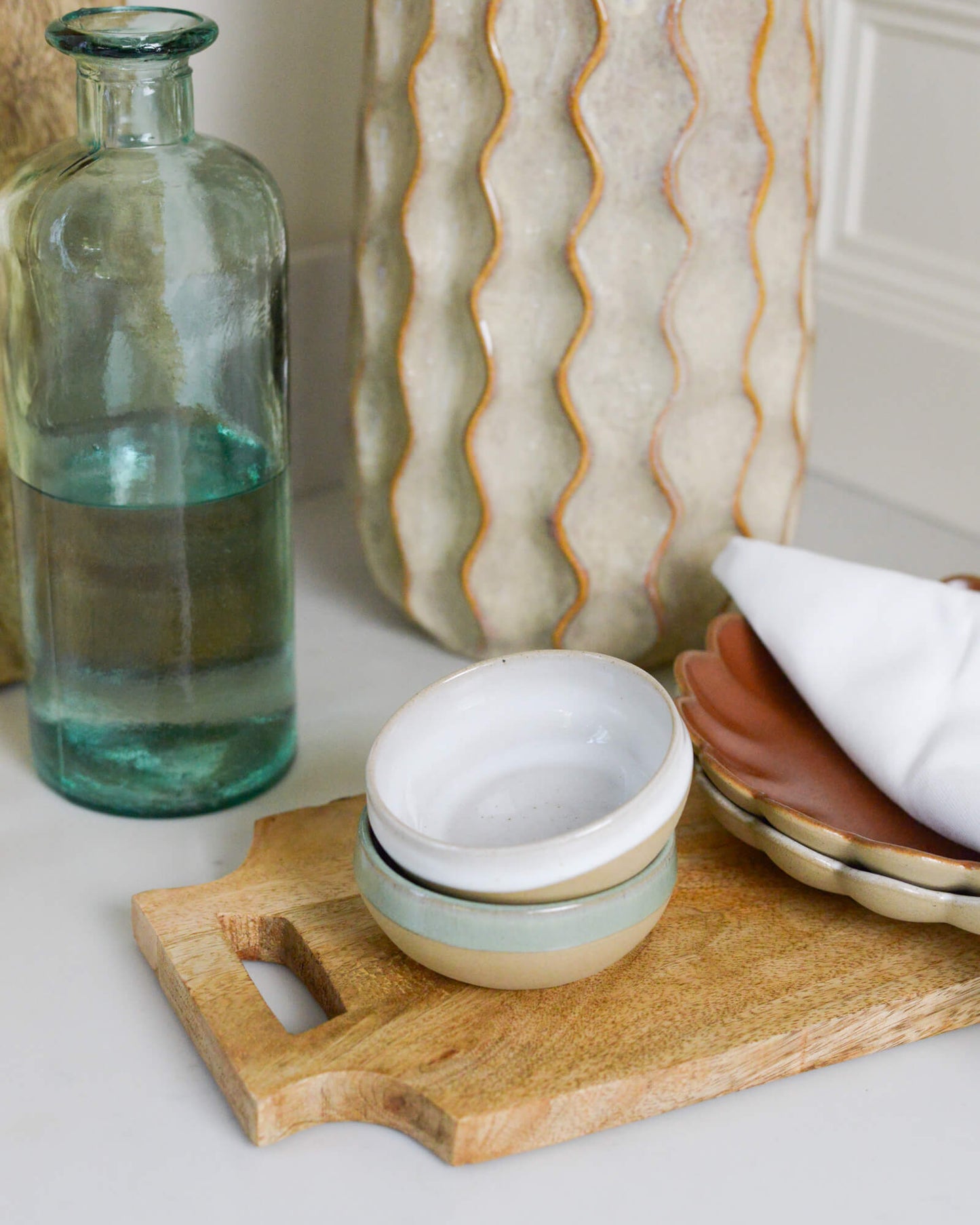 Decorative items including a glass bottle, ceramic dipping bowls, and a wooden cutting board on a white marble surface.