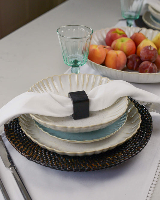 Dining table setting with plates, napkin, squared napkin ring and fruit bowl.