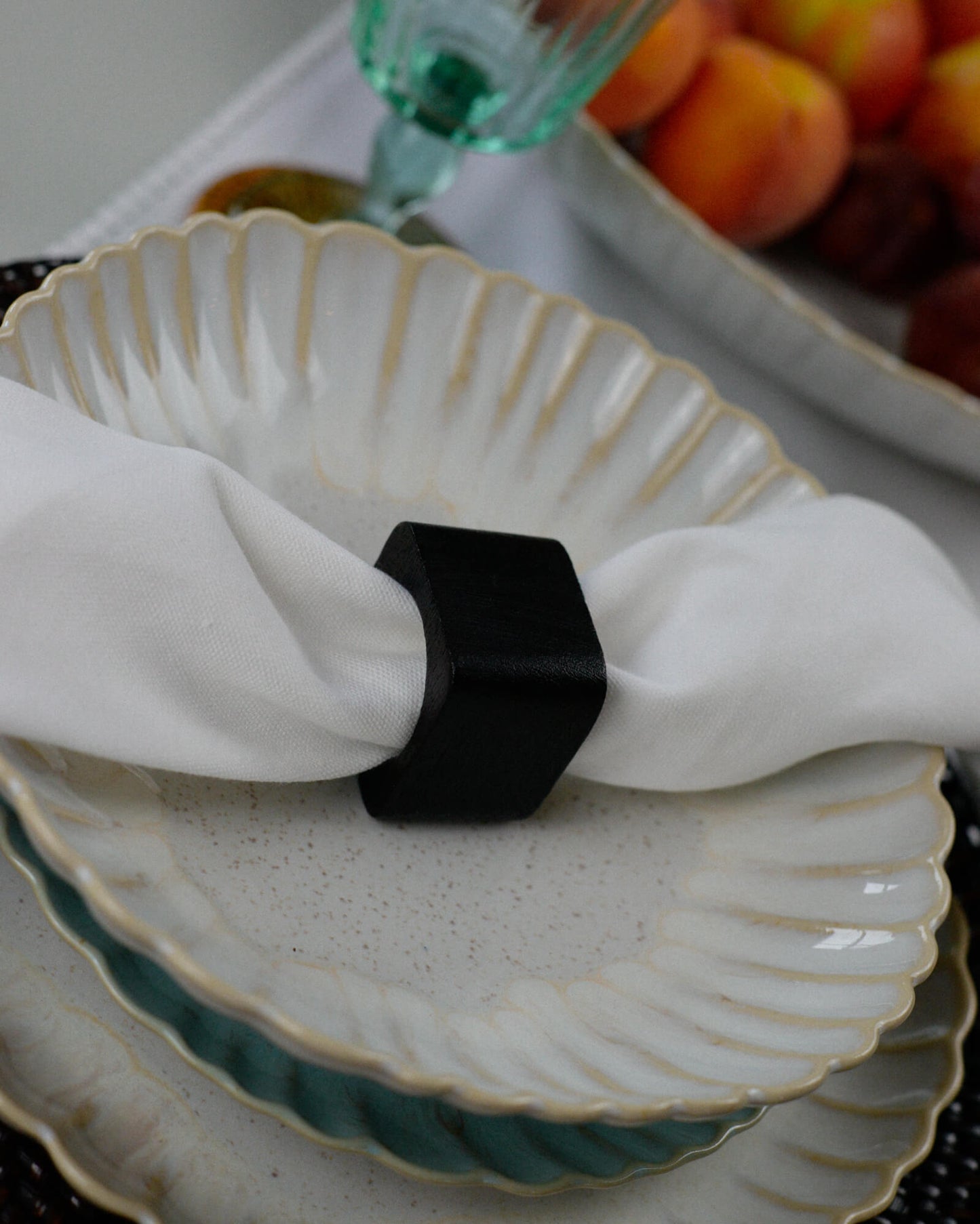 Decorative plate with a white napkin and dark wood napkin ring, with fruits in the background.