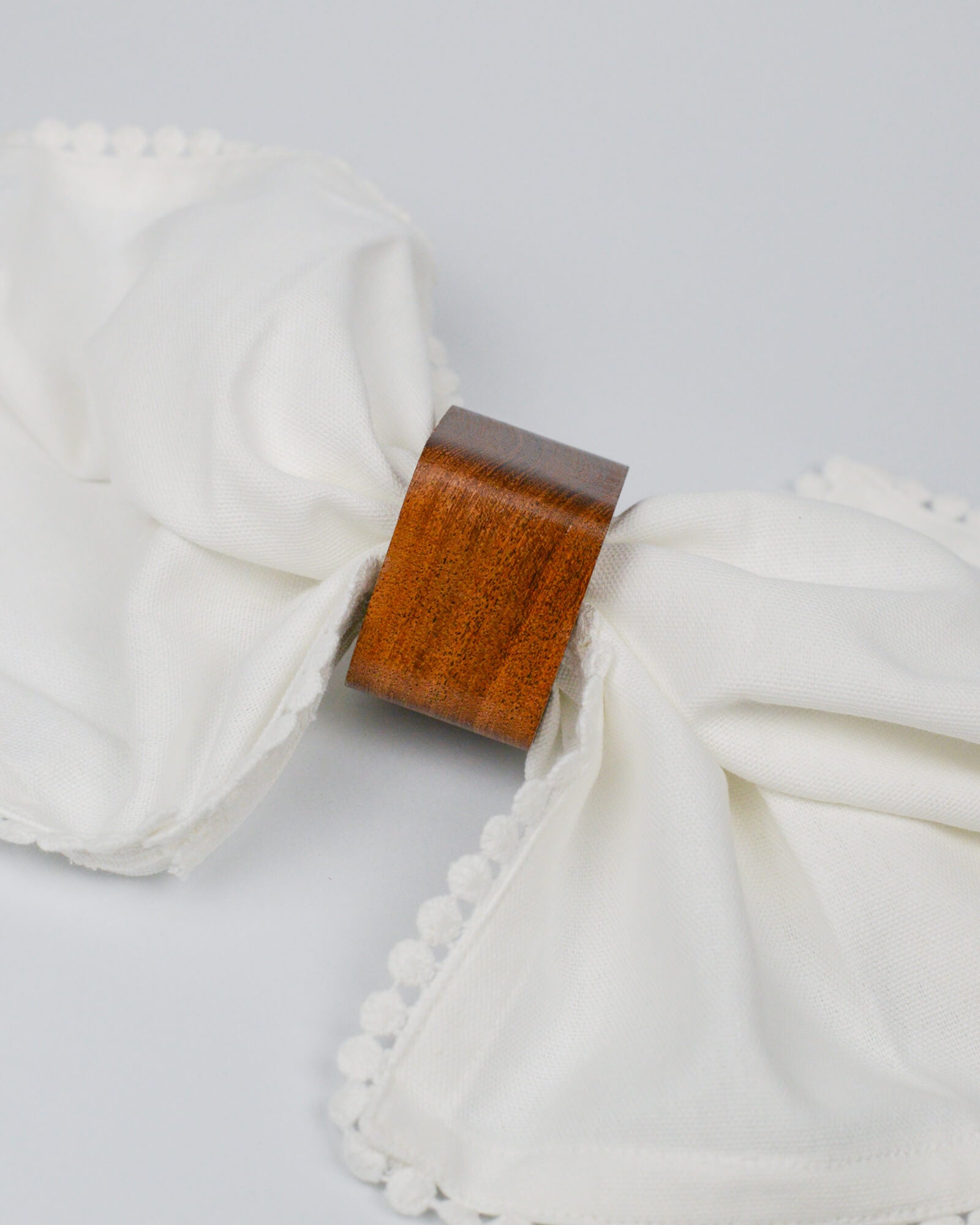 Close-up of a wooden napkin ring with white cotton napkin pom-pom edging on a white background