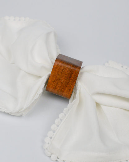 Close-up of a wooden napkin ring with white cotton napkin pom-pom edging on a white background
