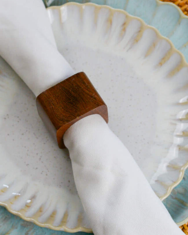 Wooden napkin ring on a white napkin with a scalloped edge plate in the background