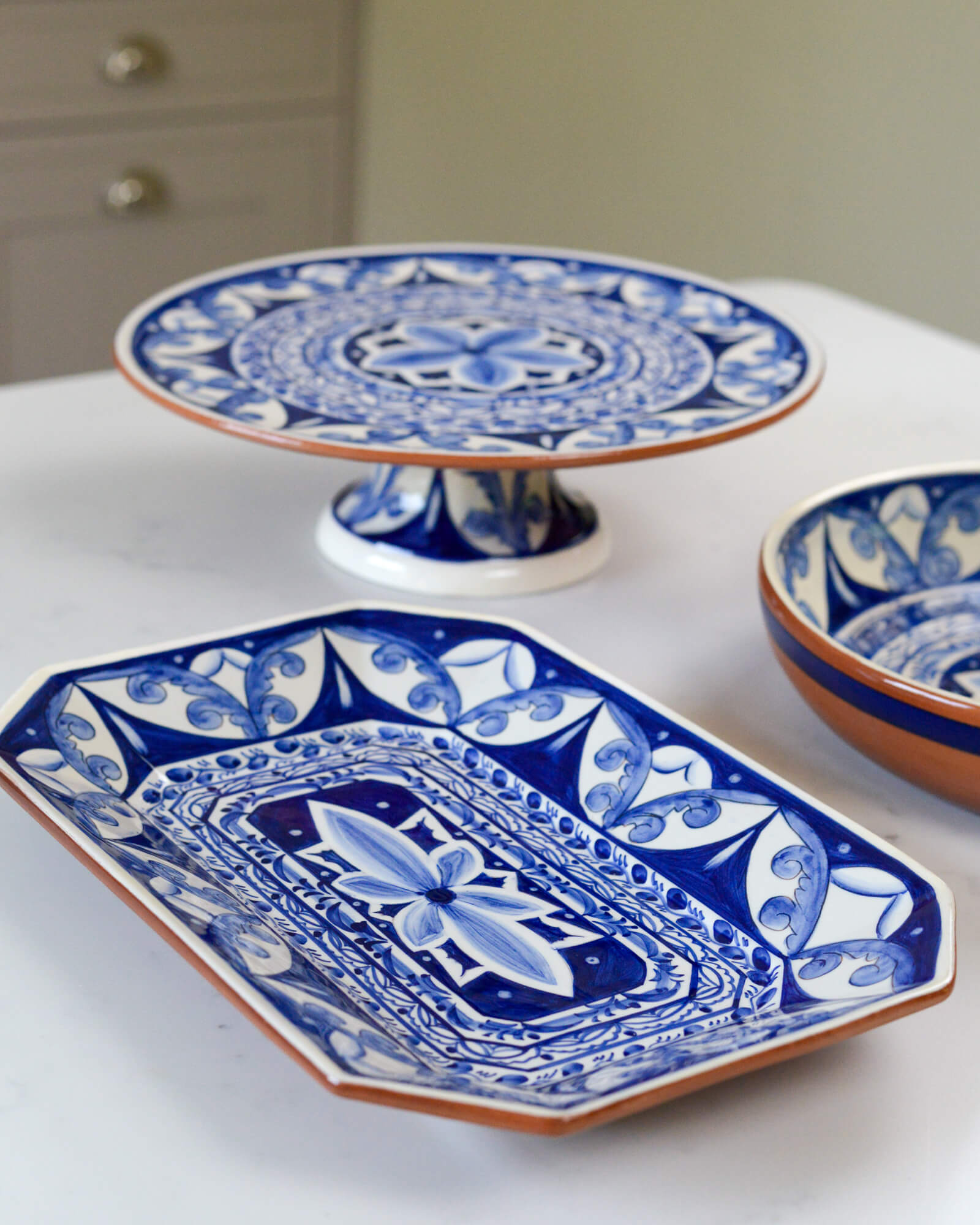 Set of blue and white ceramic terracotta dishes and a cake stand on a white marble surface
