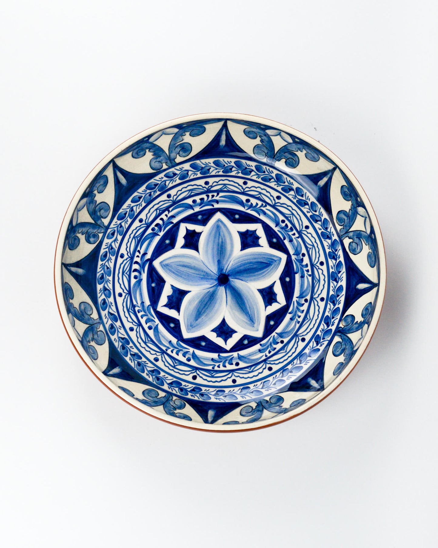 Decorative terracotta serving bowl with blue floral design on a white background
