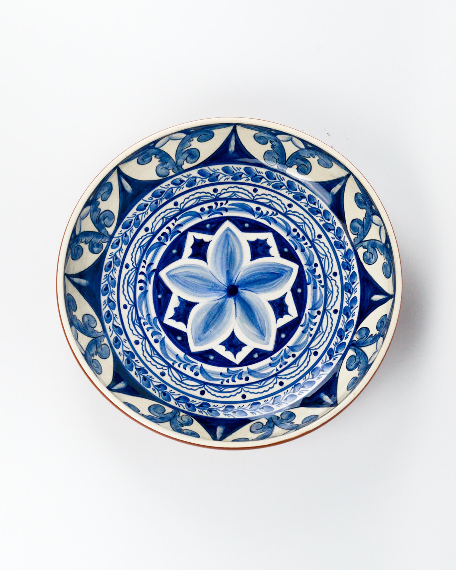 Decorative terracotta serving bowl with blue floral design on a white background
