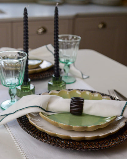 Dining table setting with green scalloped edge plates, recycled glass glasses, and black taper candles.