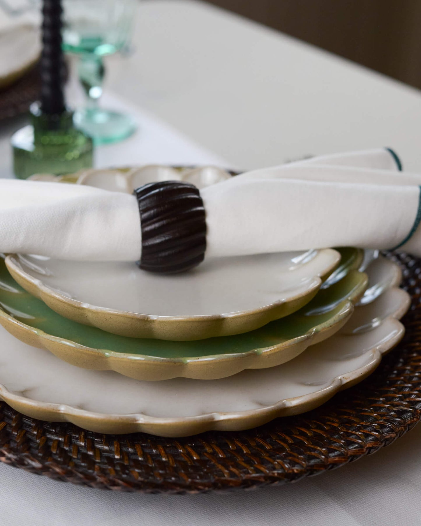 Stack of ceramic scalloped edge plates with a dark wooden carved napkin ring on a table