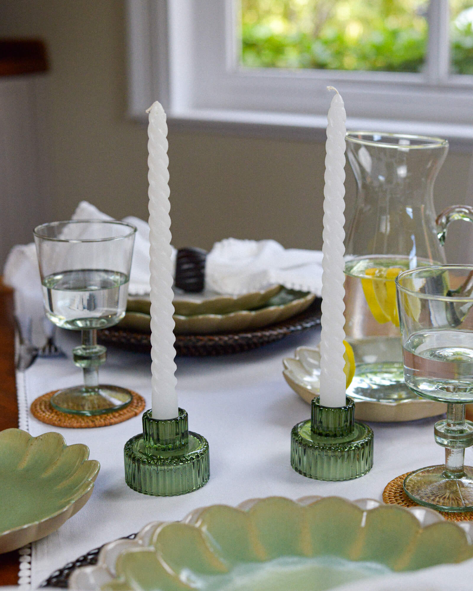 Decorative table setting with green candle holders and white twisted taper candles on a white tablecloth.
