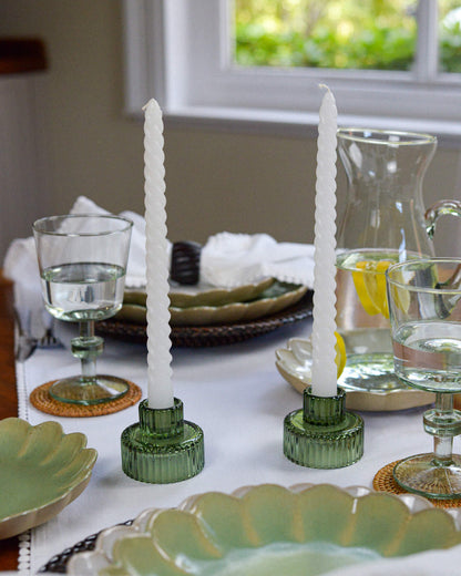 Decorative table setting with green candle holders and white twisted taper candles on a white tablecloth.