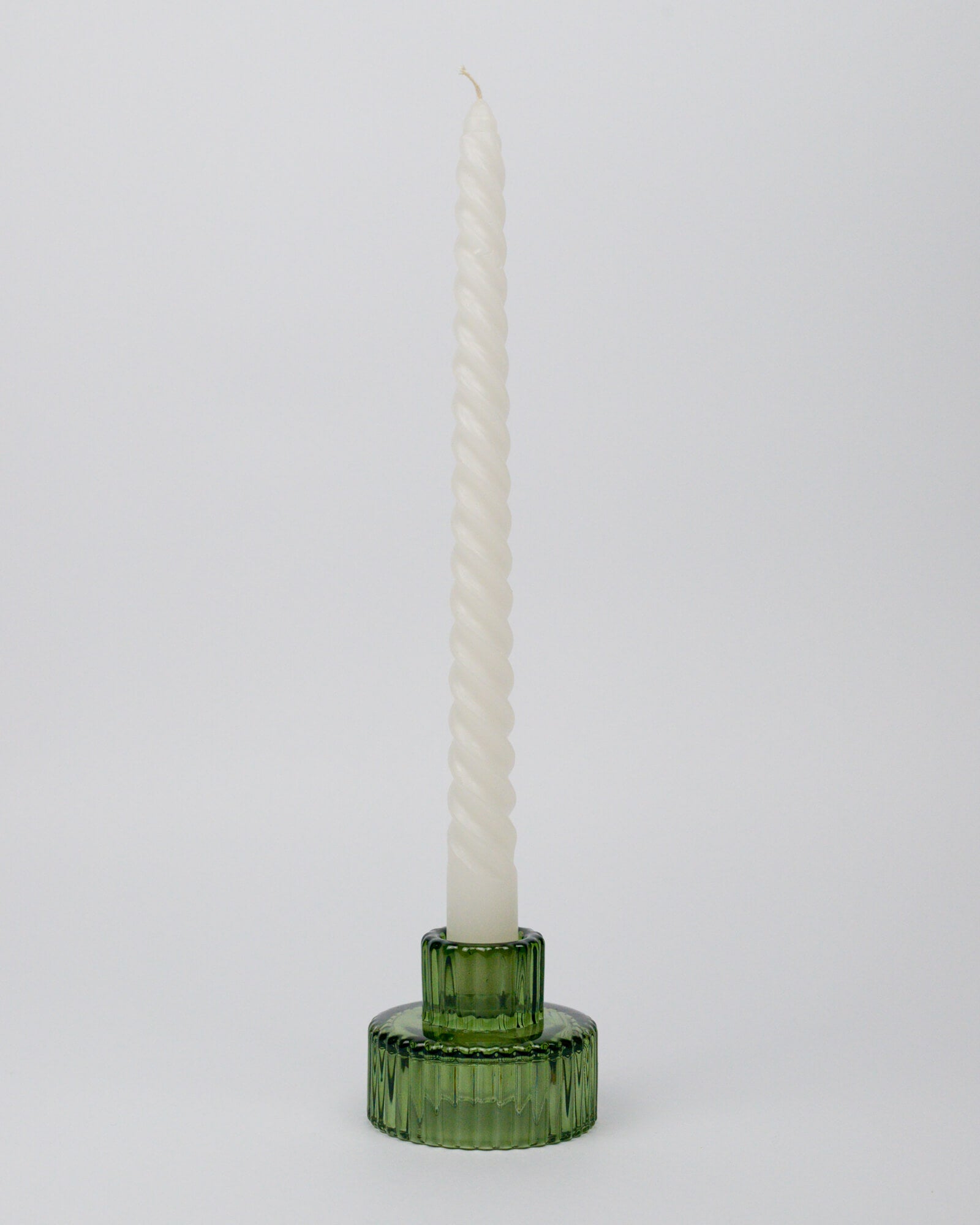Green candle holder with a twisted white taper candle on a white background