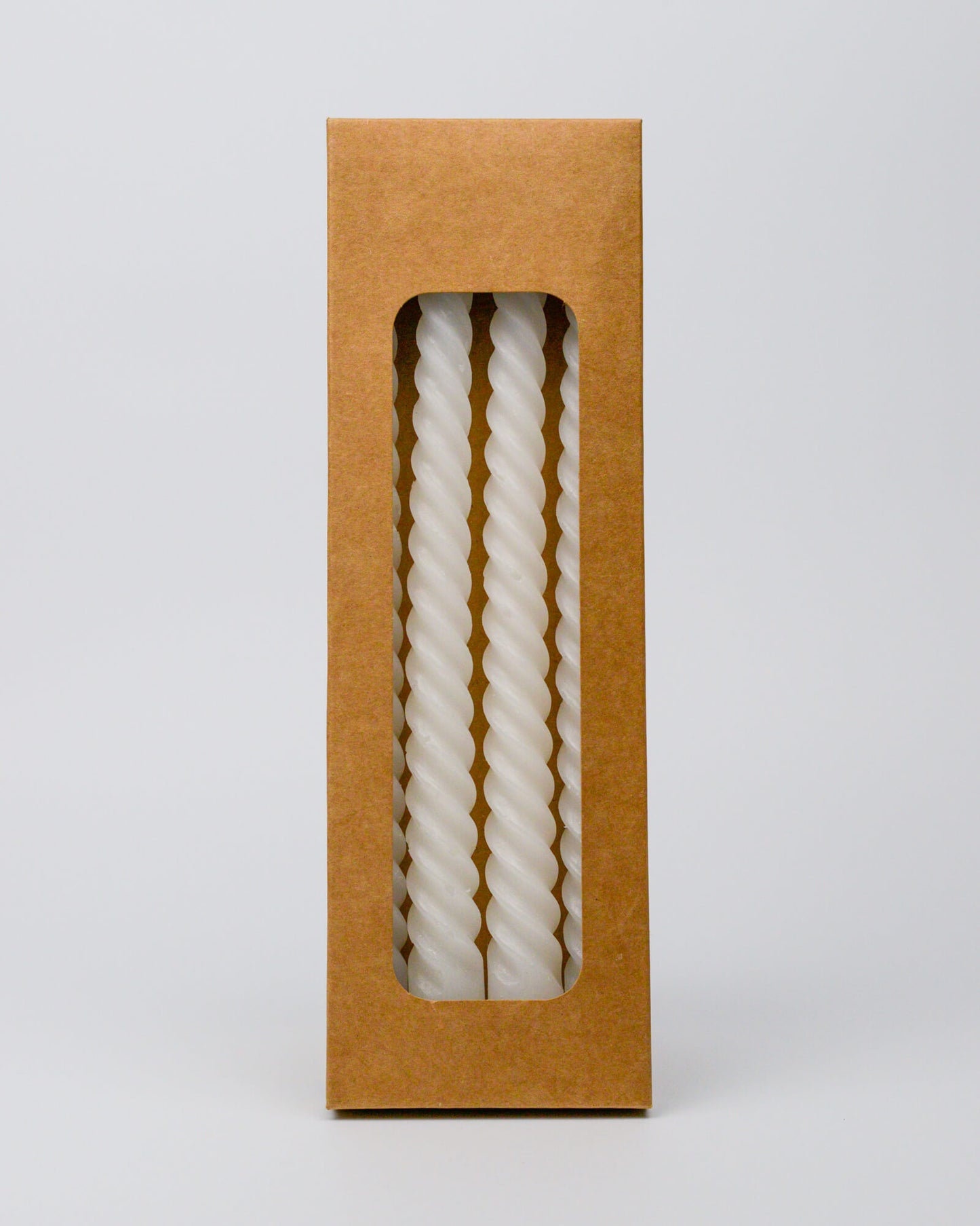 Twisted white taper candle in a brown cardboard box on a white background
