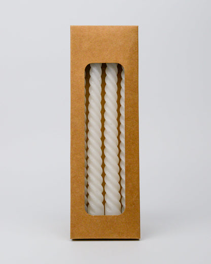 Twisted white taper candle in a brown cardboard box on a white background
