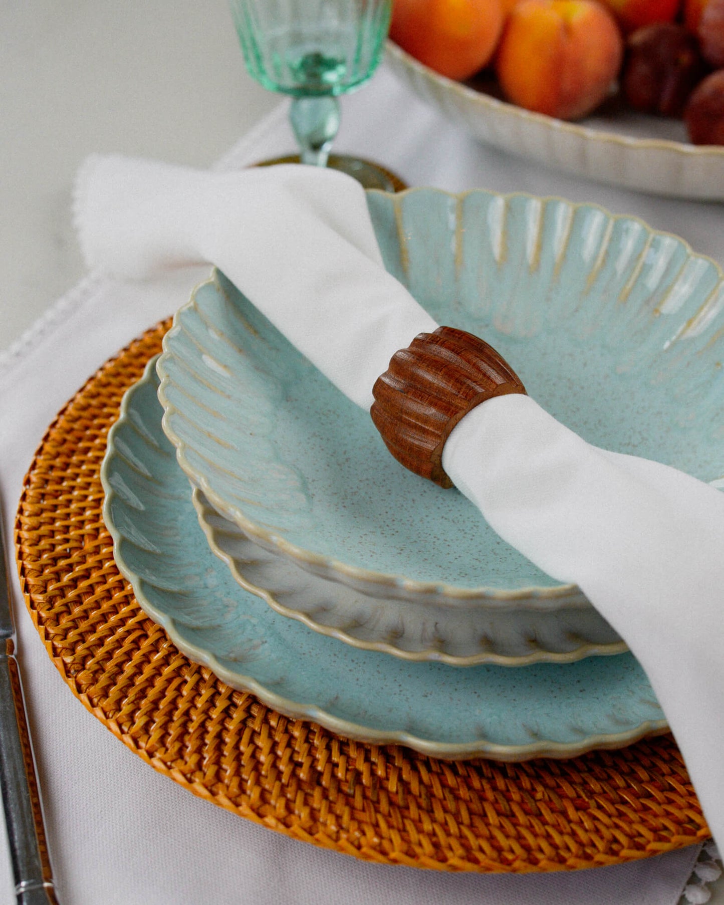 Light blue ceramic plates with a white linen napkin and brown wooden twisted napkin ring on a woven placemat.