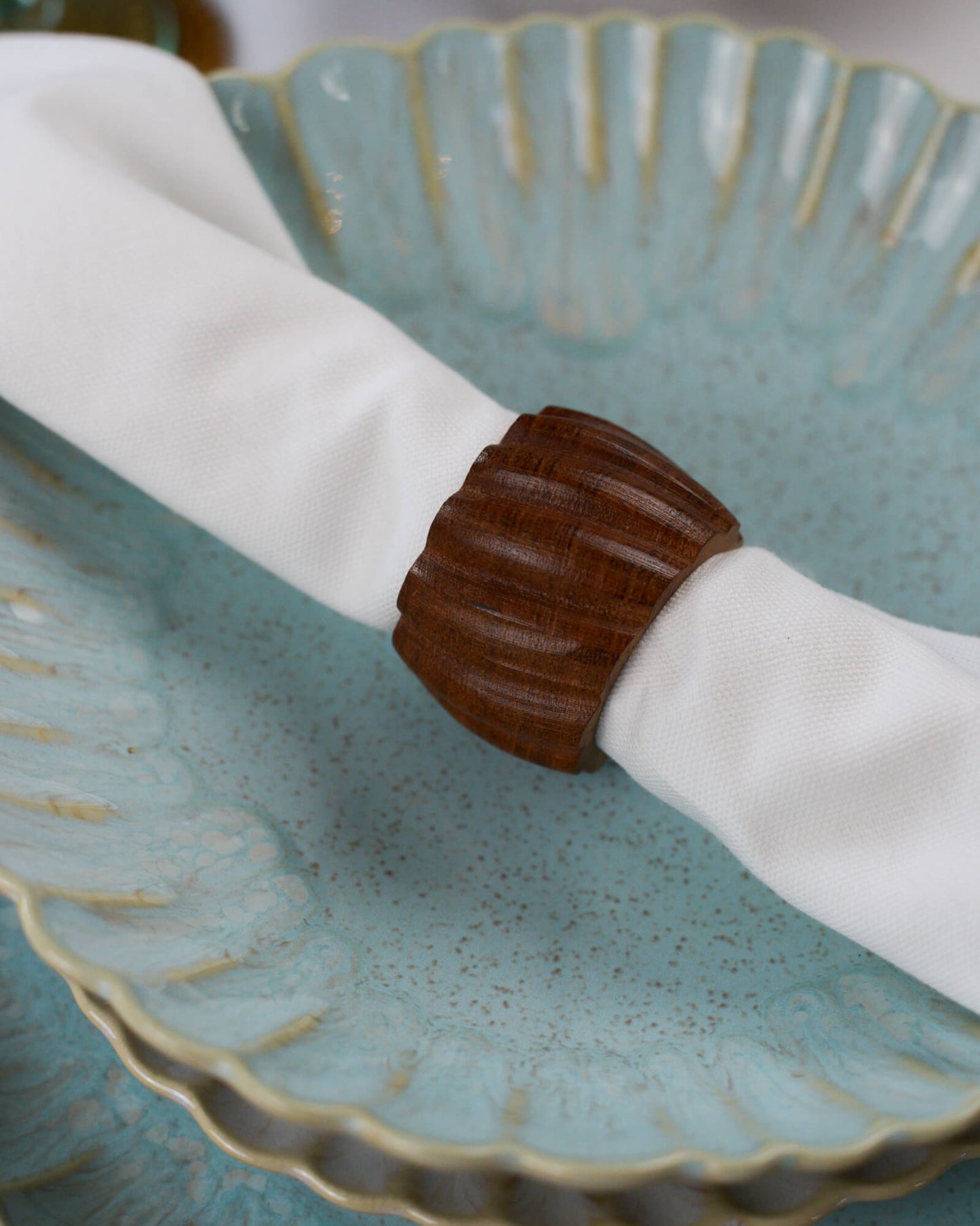 Brown wooden napkin ring on a white napkin over a blue ceramic dish