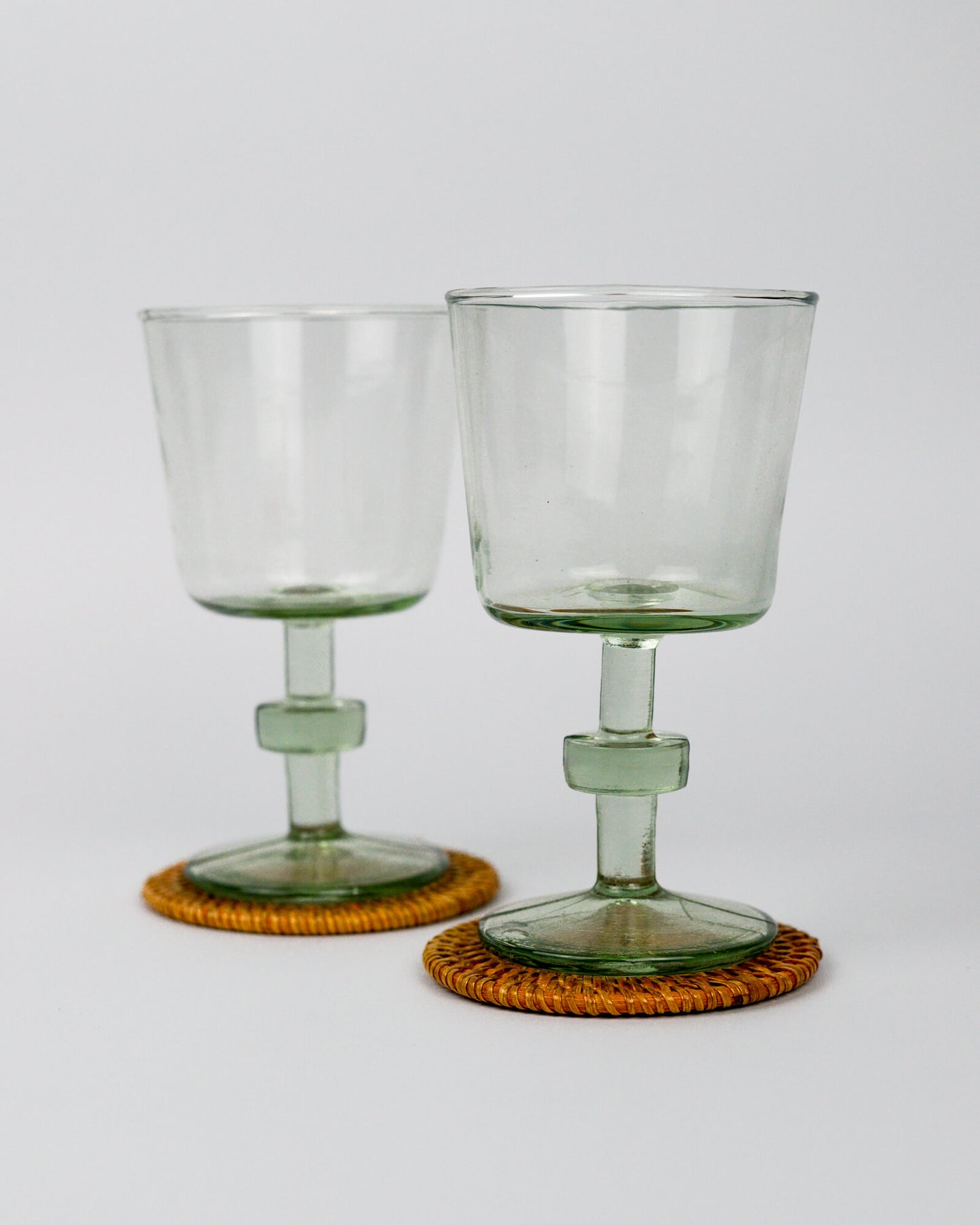 Two clear glass goblets on woven coasters with a white background