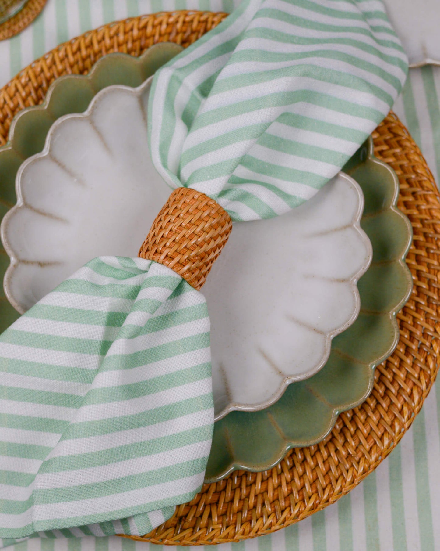 Green and white striped napkin on a scalloped plate with a woven placemat.