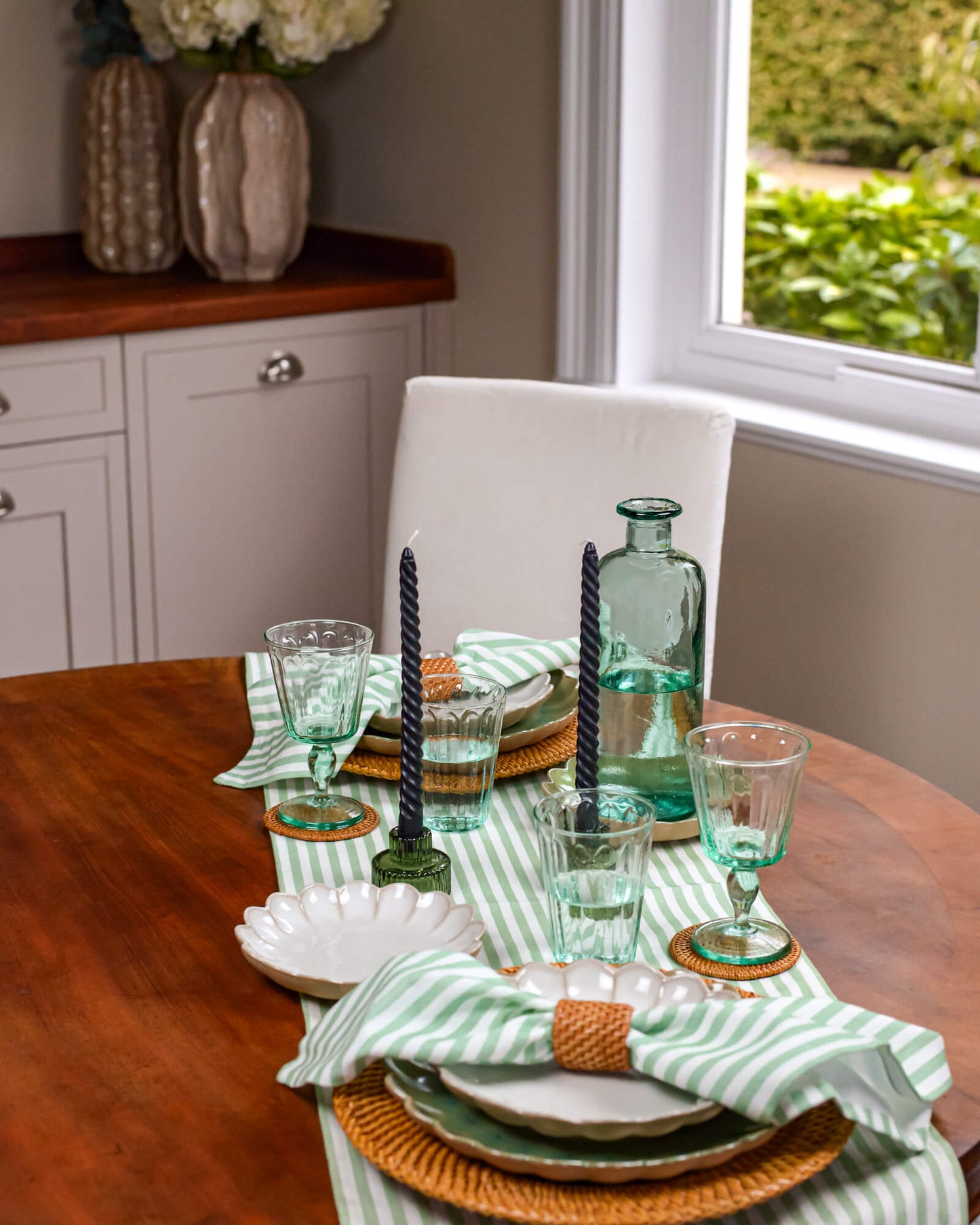 Dining table set with green glasses, candles, and striped napkins in a home setting.