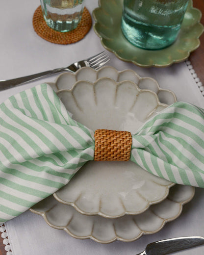Scalloped edge plate with green and white striped napkin and woven rattan napkin ring on a white tablecloth.