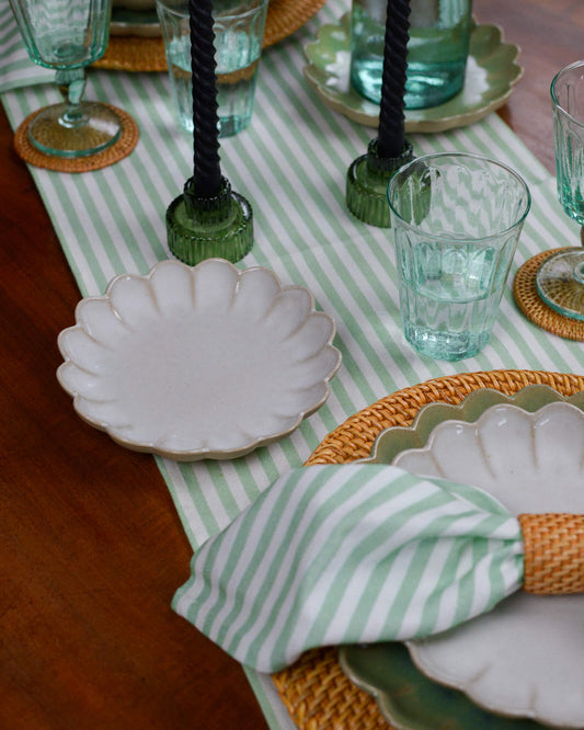 Table setting with green and white striped table runner, white plates, and decorative napkins.